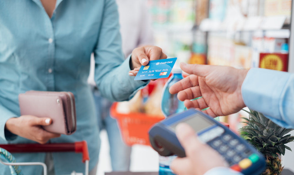 A woman handing out a credit card to a merchant to illustrate the concept of how credit and loan can help you go further in life