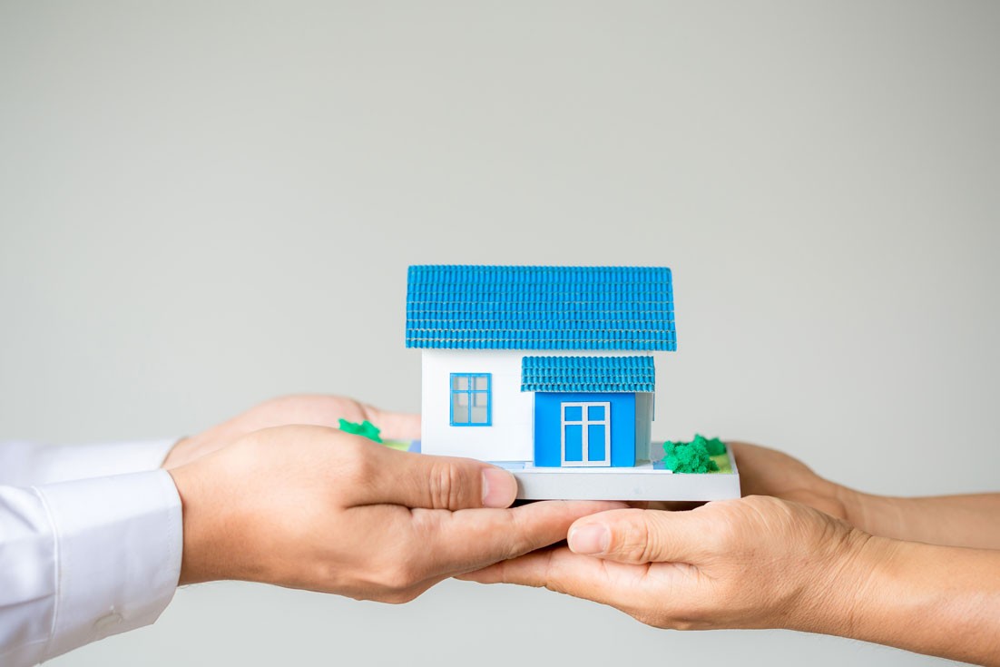 An image of a person passing a house model to another person to illustrate bridging loans from licensed moneylenders in Singapore